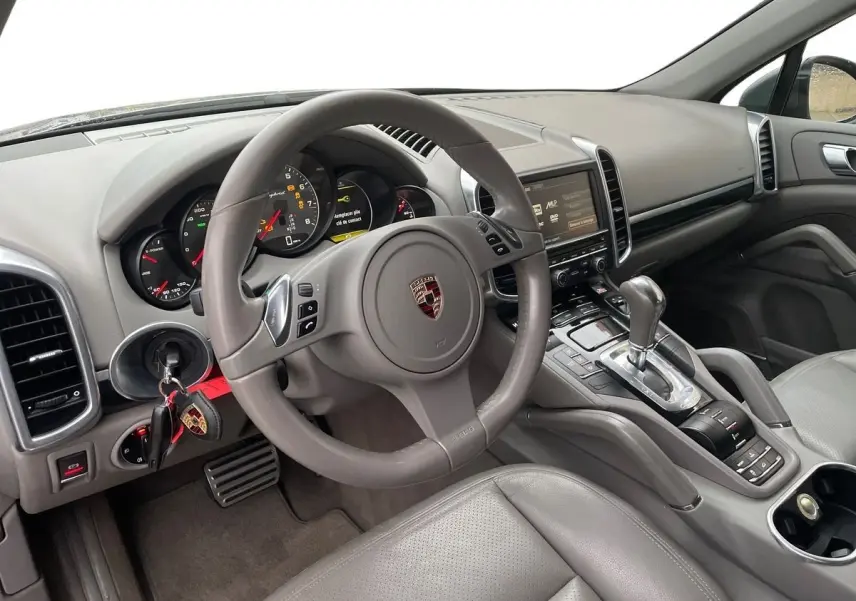 Intérieur gris clair du Porsche Cayenne S Hybrid 2010 vu côté conducteur, volant multifonction et console centrale avec levier automatique.