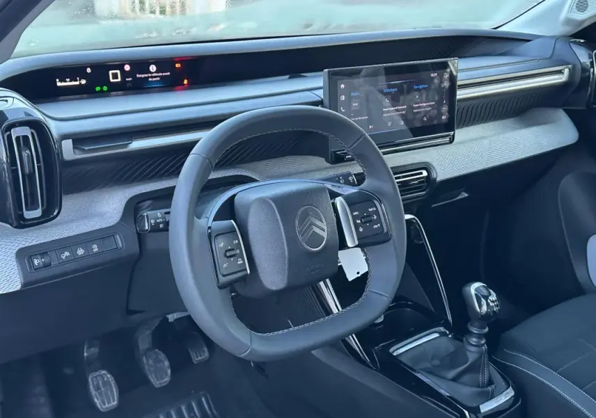 Vue intérieure avant de la Citroën C3 2025 noire, volant multifonction, écran tactile et levier de vitesse manuel visibles.