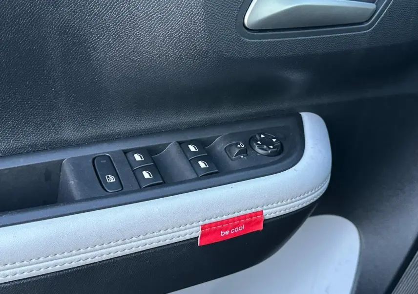 Gros plan sur la commande des vitres et rétroviseurs côté conducteur de la Citroën C3 noire avec étiquette rouge "be cool" sur la garniture.