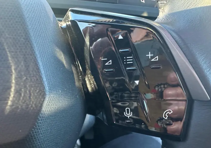 Gros plan sur les commandes au volant noir brillant du Peugeot 3008 blanc Hybrid 145 e-DCS6 Allure 2025.