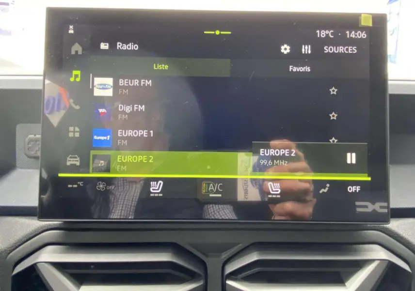 Écran tactile central du Dacia Duster 2025 affichant la radio FM avec commandes de climatisation et sièges chauffants visibles.