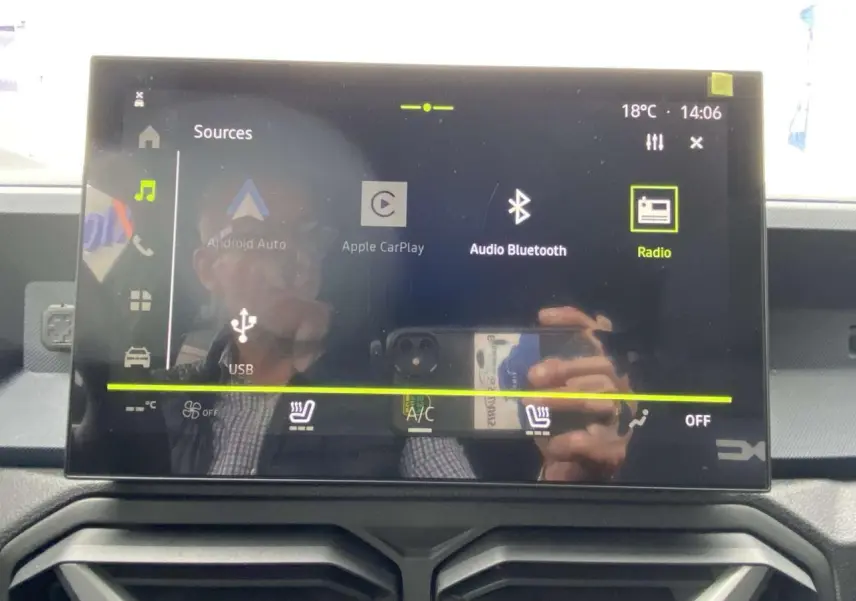 Écran tactile central du Dacia Duster 2025 affichant les options multimédia et climatisation, avec reflet partiel.