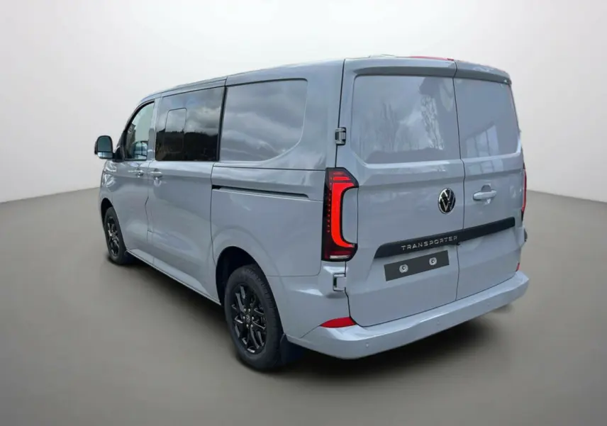 Vue 3/4 arrière droite d’un Volkswagen Transporter TDI 170 DSG ProCab L1 gris Stone avec vitres teintées et jantes alu noires.
