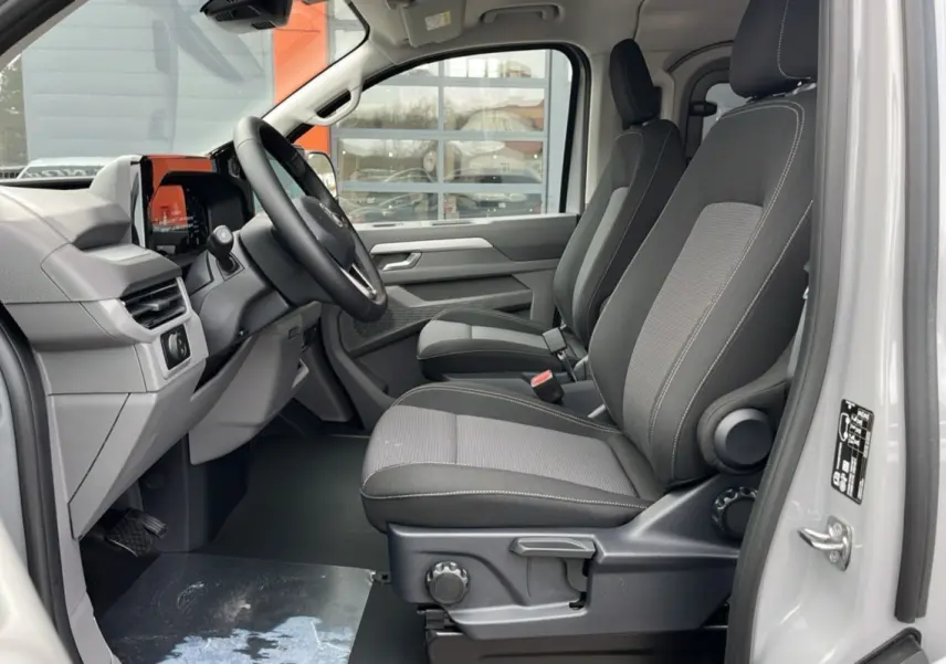 Vue intérieure côté conducteur du Volkswagen Transporter TDI 170 DSG ProCab L1 gris Stone, sièges tissu noir et tableau de bord moderne.