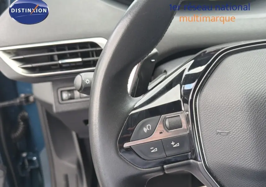 Gros plan sur le volant multifonction noir du Peugeot 5008 bleu Célèbes, avec commandes audio et téléphone visibles.