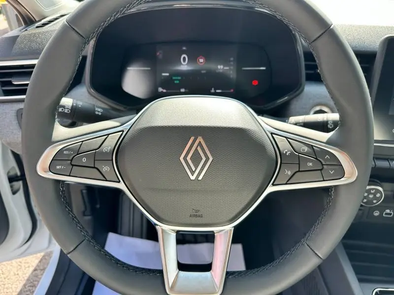 Volant multifonction noir avec logo Renault au centre, tableau de bord numérique en arrière-plan dans une Renault Clio blanche.
