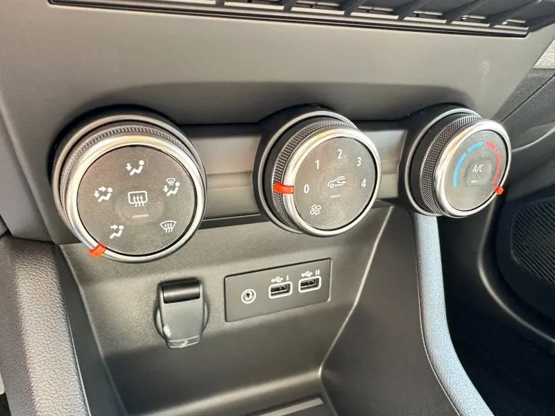 Gros plan sur les commandes de climatisation noires et les ports USB du tableau de bord d'une Renault Clio Blanc Glacier 2025.