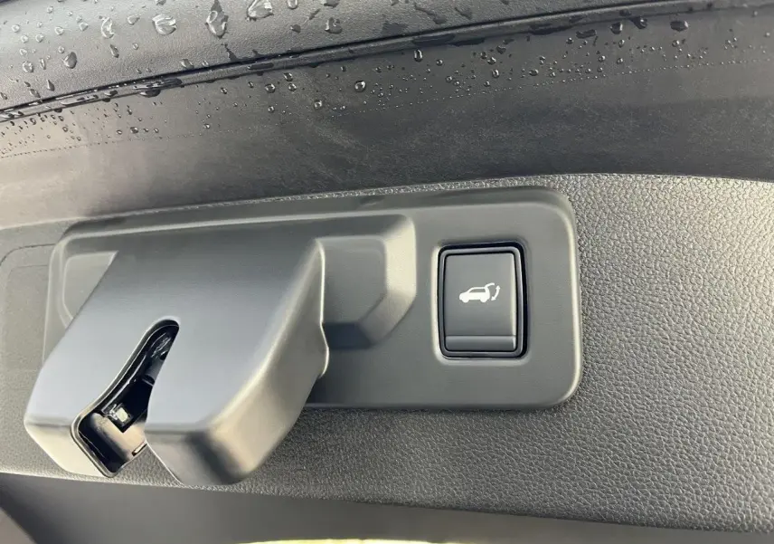 Gros plan sur la poignée intérieure de coffre avec bouton d’ouverture, sur Renault Austral gris schiste 2025.