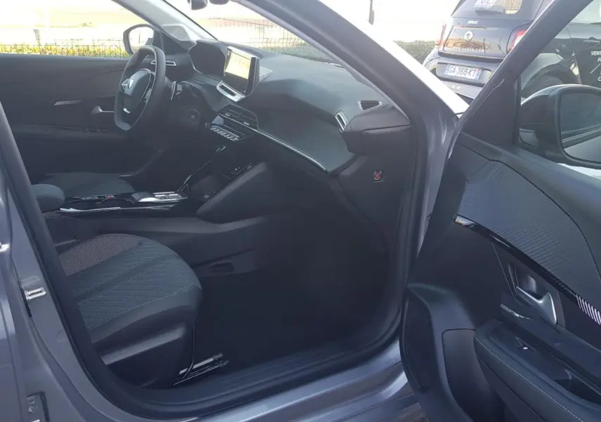 Vue intérieure côté conducteur d'une Peugeot 208 gris 2025, mettant en valeur le tableau de bord et l'écran tactile.
