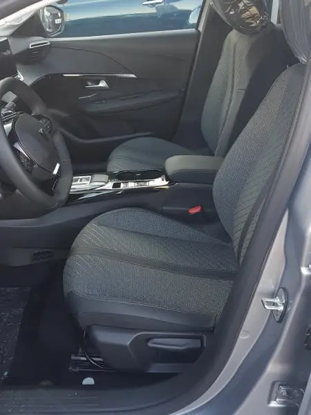 Vue intérieure côté conducteur de la Peugeot 208 Hybrid 110 gris, sièges tissu et volant réglable visibles.