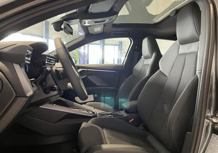 Vue intérieure côté conducteur de l’Audi A3 Sportback gris, sièges sport S line en cuir avec logo embossé et toit ouvrant panoramique.
