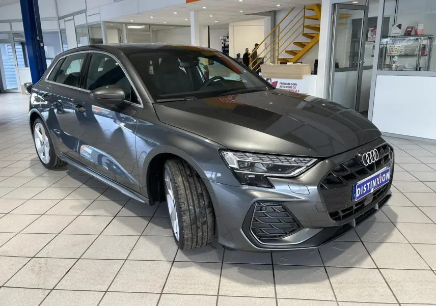 Audi A3 Sportback gris métallisé vue 3/4 avant en intérieur avec calandre noire et jantes 5 branches en Y.