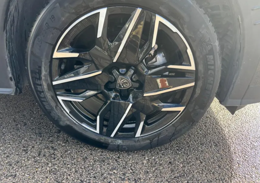 Gros plan sur la jante alliage noire et argent de 19 pouces du Peugeot 3008 Hybrid gris, avec pneu Michelin visible.