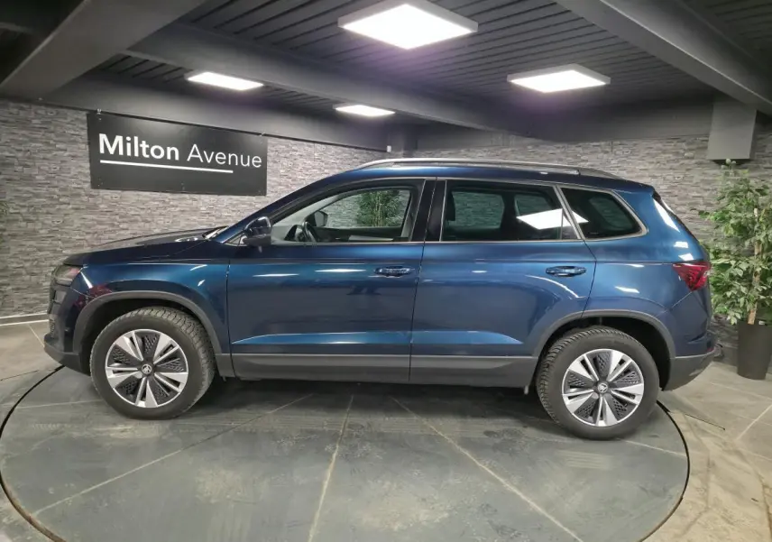 Vue latérale droite d'un Skoda Karoq bleu métallisé 2024 en showroom avec jantes alliage 17 pouces.