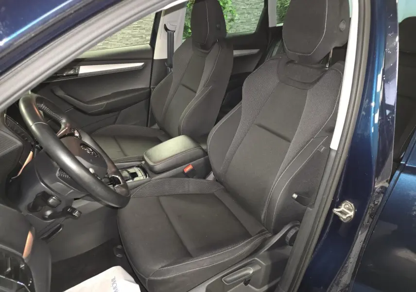 Vue intérieure côté conducteur du Skoda Karoq bleu 2024, sièges tissu noir avec accoudoir central et volant cuir.