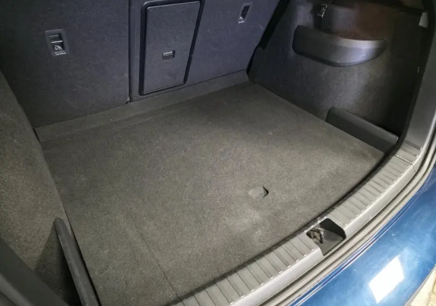 Vue plongeante sur le coffre spacieux et propre du Skoda Karoq bleu 2024, avec moquette noire et trappe centrale.