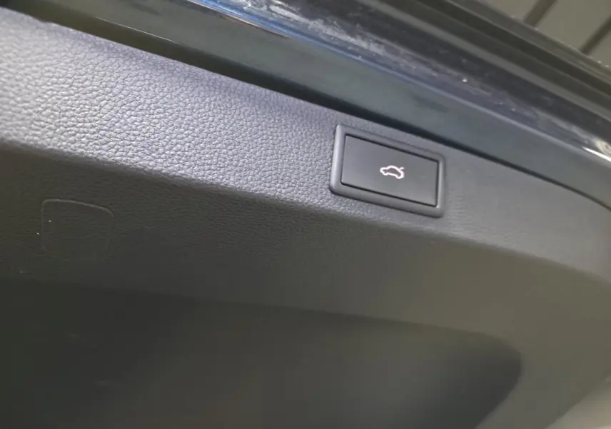 Gros plan sur le bouton d'ouverture électrique du hayon du Skoda Karoq bleu, intérieur du coffre visible.