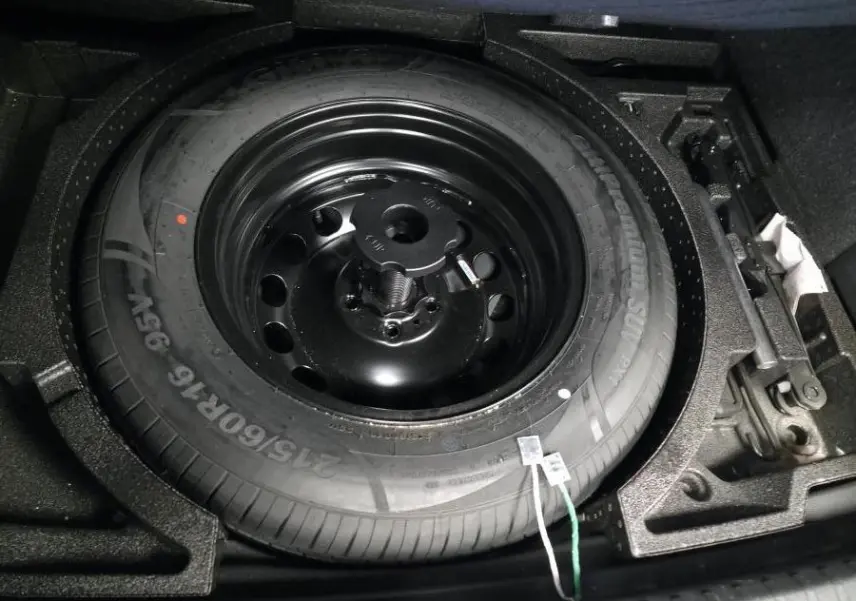 Gros plan sur la roue de secours temporaire noire dans le coffre du Skoda Karoq bleu 2024.