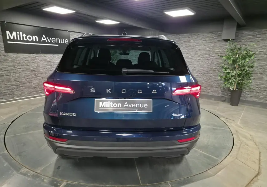 Vue arrière d'un Skoda Karoq bleu métallisé 2024 avec feux LED et logo SKODA visible sur fond intérieur showroom.