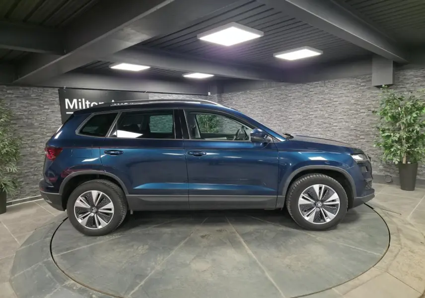 Vue latérale droite d'un Skoda Karoq bleu métallisé 2024 dans un showroom avec jantes alliage 17 pouces.
