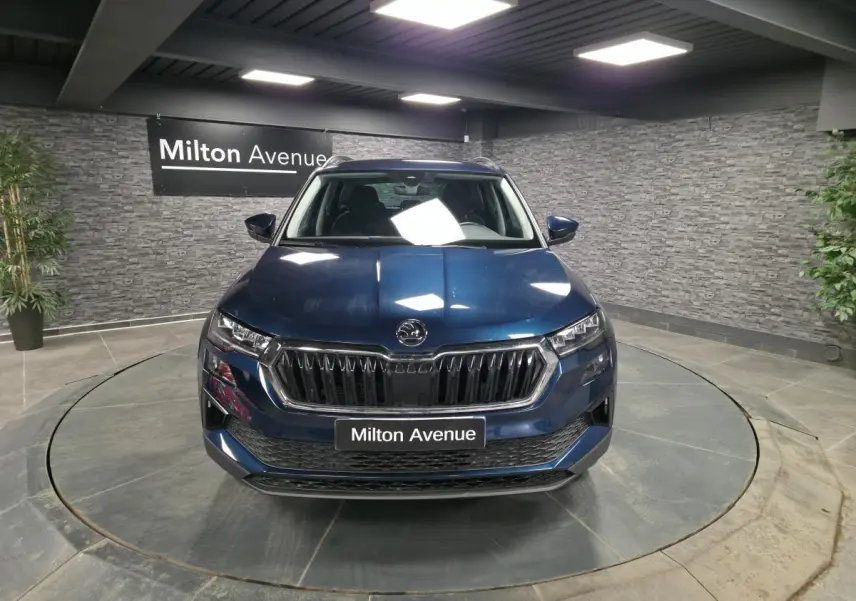 Vue frontale d'un Skoda Karoq bleu métallisé 2024 dans un showroom avec calandre noire et logo central.