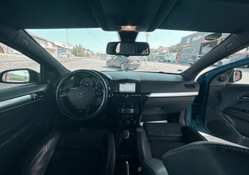 Vue intérieure frontale de l’Opel Astra OPC 2008 avec tableau de bord noir et volant cuir, porte passager ouvert.