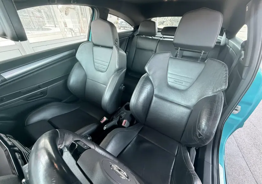 Vue intérieure avant droite sur les sièges baquets noirs Recaro d’une Opel Astra OPC bleu visible à l’ouverture de la porte.