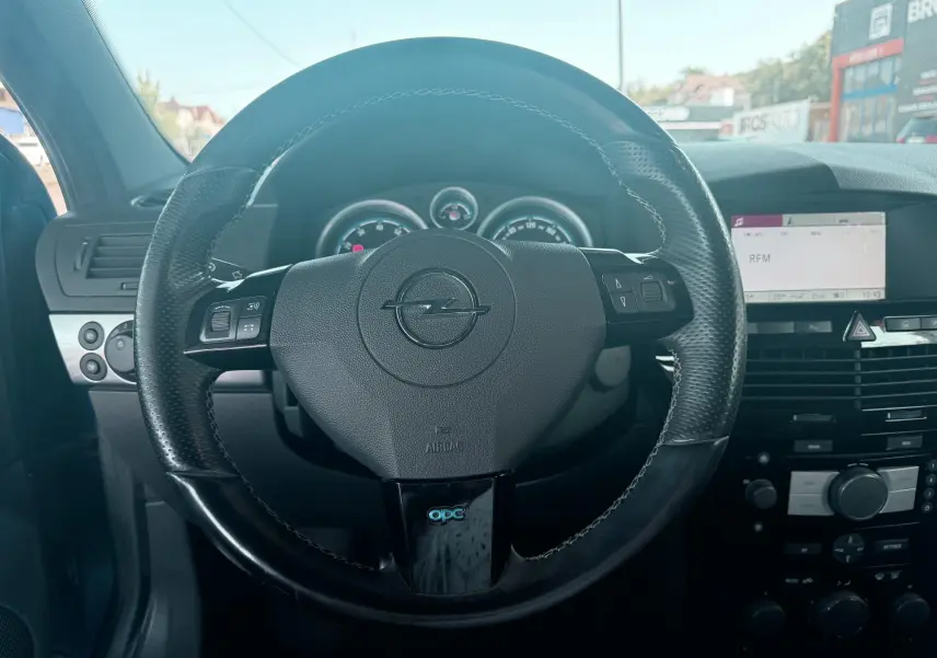 Vue intérieure centrée sur le volant noir perforé de l'Opel Astra OPC 2008 avec tableau de bord et écran multimédia.