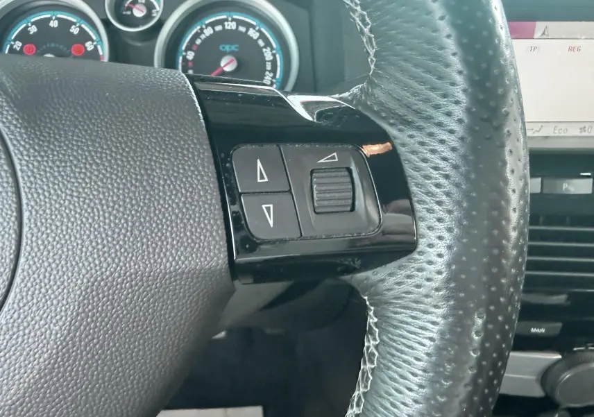 Gros plan sur le volant en cuir noir de l’Opel Astra OPC 2008 avec commandes intégrées et compteurs en arrière-plan.