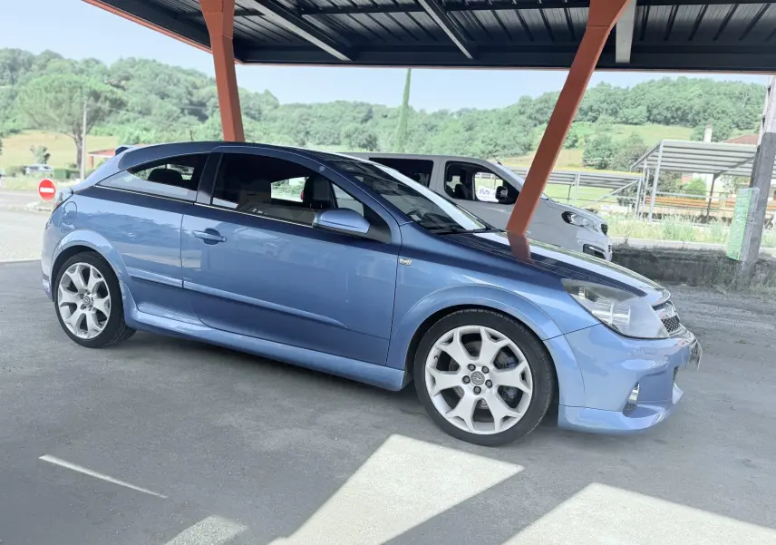Vue de profil côté gauche d'une Opel Astra OPC 2.0i bleu métallisé sous abri avec jantes sport blanches.