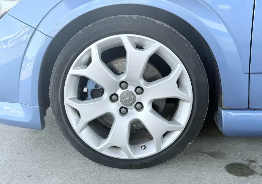 Gros plan sur la roue avant gauche argentée d’une Opel Astra OPC bleue, avec frein à disque visible.
