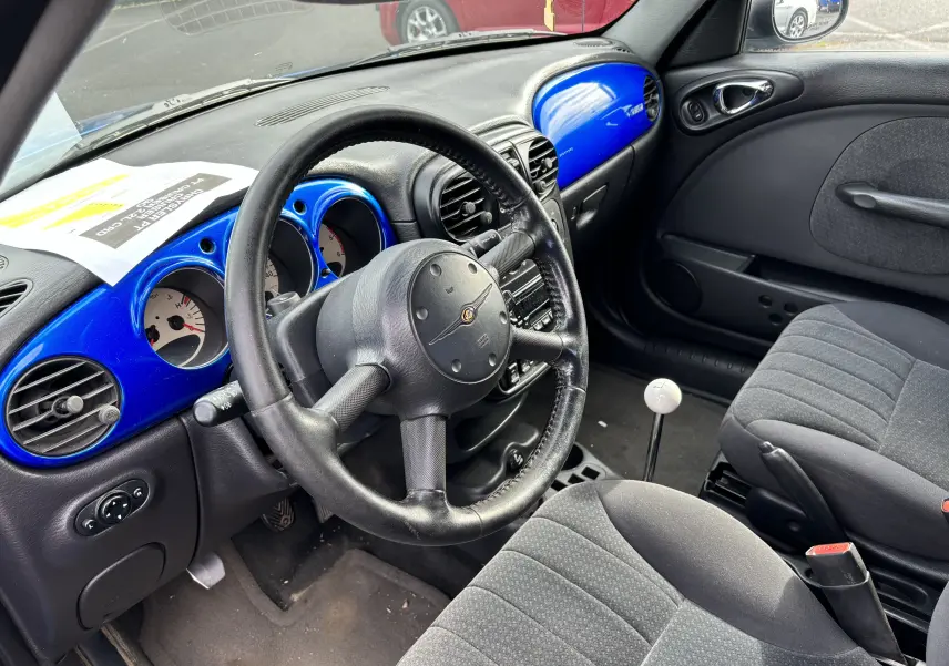 Vue intérieure côté conducteur du Chrysler PT Cruiser 2004, tableau de bord bleu vif et levier de vitesse manuel blanc.