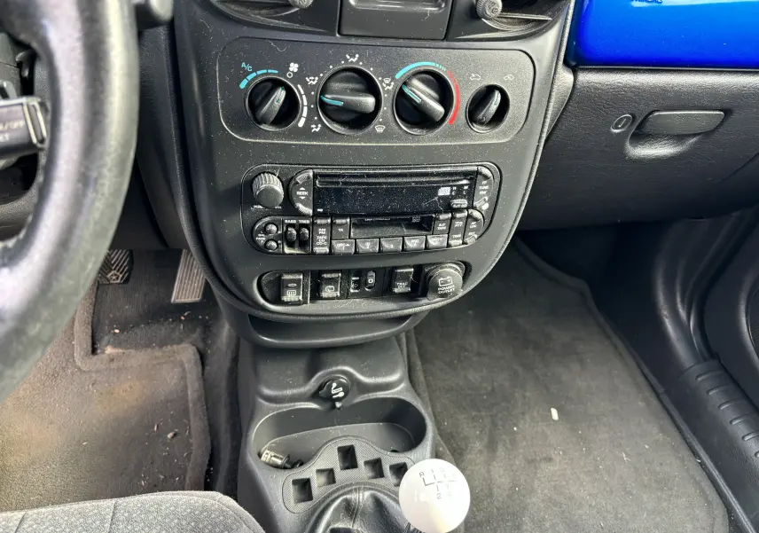 Vue intérieure centrée sur la console centrale et levier de vitesse manuel blanc du Chrysler PT Cruiser bleu de 2004.