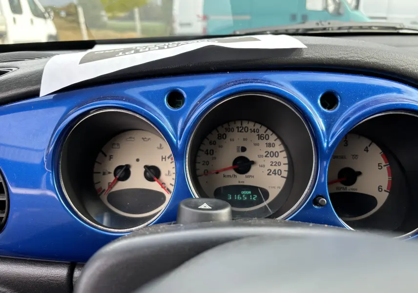 Tableau de bord bleu métallique du Chrysler PT Cruiser 2004, vue centrée sur les compteurs et le volant partiel.