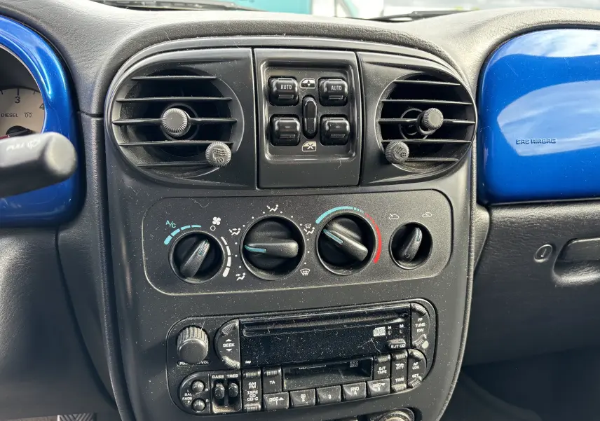 Tableau de bord bleu et noir du Chrysler PT Cruiser 2004, vue frontale centrée sur commandes de climatisation et radio.