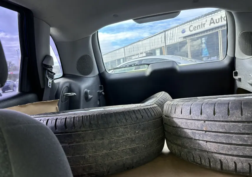 Intérieur arrière du Chrysler PT Cruiser bleu 2004 avec deux pneus usés posés dans le coffre, vue vers la lunette arrière.
