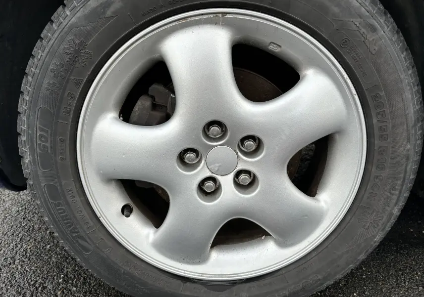 Gros plan sur la roue avant droite d'un Chrysler PT Cruiser bleu 2004, mettant en valeur le pneu hiver marqué 205/55 R16.