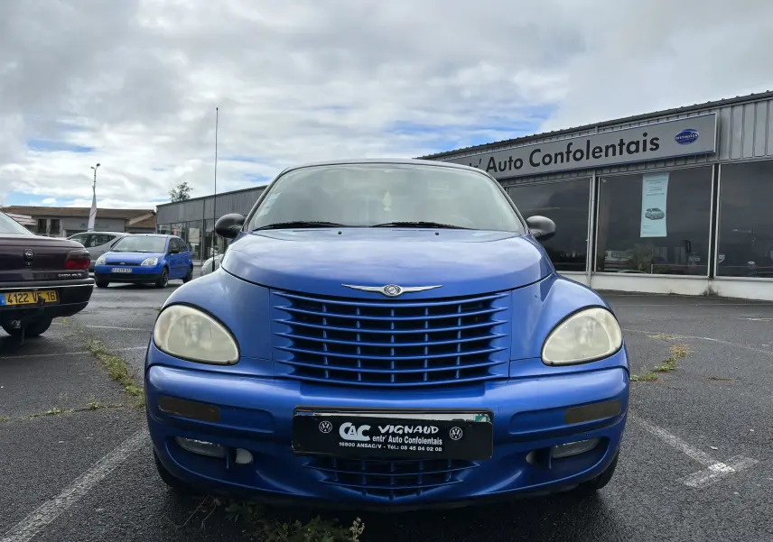 Vue frontale d'une Chrysler PT Cruiser bleue garée devant un garage Auto Confolentais par temps nuageux.