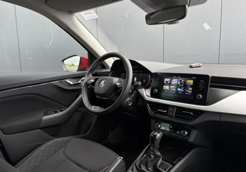 Intérieur du Skoda Kamiq TSI 110 DSG Ambition 2024, vue côté conducteur, volant cuir et écran tactile central visible.