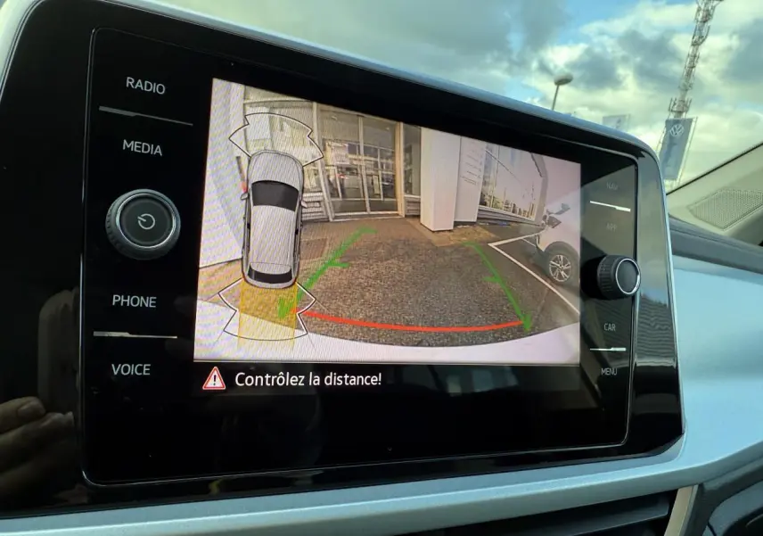 Écran tactile du système infotainment montrant la caméra de recul du Volkswagen T-Roc blanc pur en stationnement.