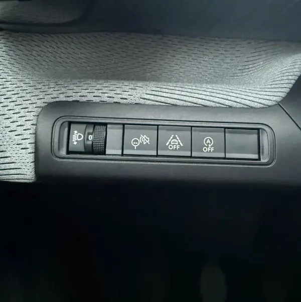 Détail des commandes intérieures sur tableau de bord de la Citroën C3 Turbo 100 ch gris, boutons réglage phares et aides à la conduite.