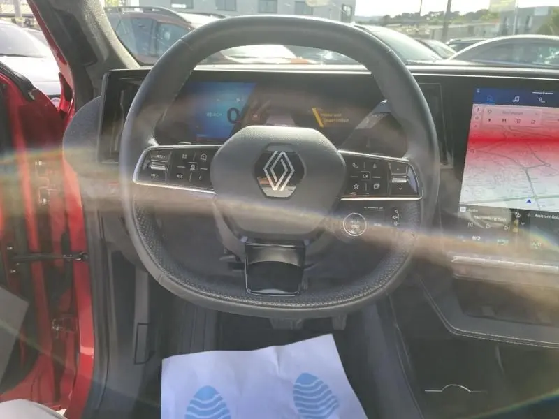 Vue intérieure centrée sur le volant du Renault Scenic E-Tech rouge flamme 2024 avec écran digital et console tactile.