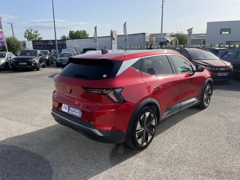 Vue 3/4 arrière droite d'un Renault Scénic E-Tech électrique 2024 rouge flamme avec jantes noires et toit noir.