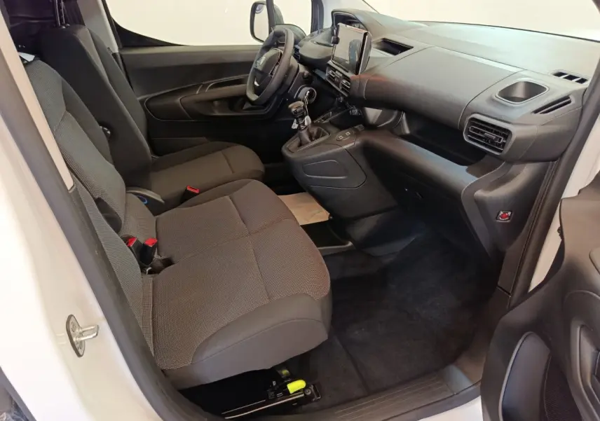 Intérieur côté conducteur du Peugeot Partner blanc 2025, montrant les sièges, tableau de bord et levier de vitesses manuel.