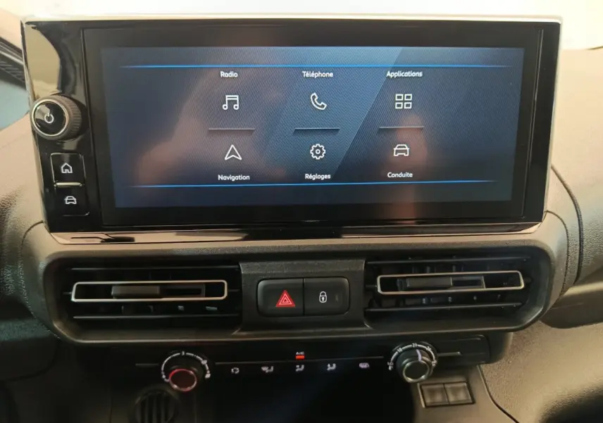 Écran tactile central du Peugeot Partner 2025 avec commandes climatisation et boutons de sécurité en vue frontale rapprochée.