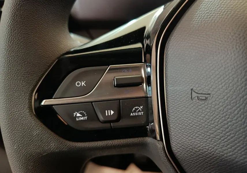 Gros plan sur les commandes à gauche du volant du Peugeot Partner blanc 2025, avec boutons de limitation et assistance.
