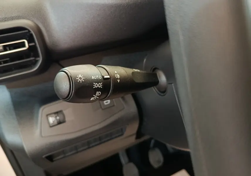 Gros plan sur la commande des phares à gauche du volant dans l’habitacle sombre d’un Peugeot Partner blanc.