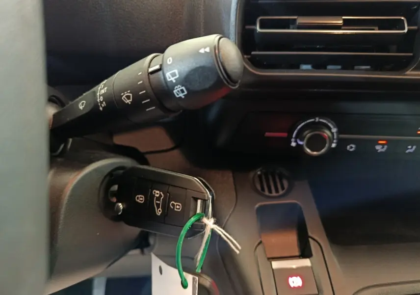 Gros plan intérieur sur la clé de contact insérée dans un Peugeot Partner blanc, avec commandes de climatisation et ventilation visibles.
