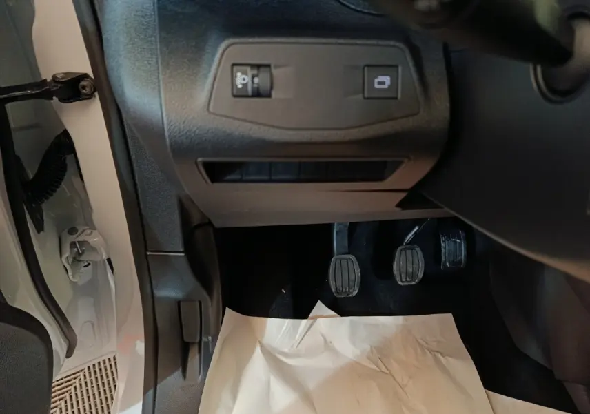 Vue intérieure côté conducteur du Peugeot Partner blanc 2025, montrant les pédales et commandes sous le tableau de bord.