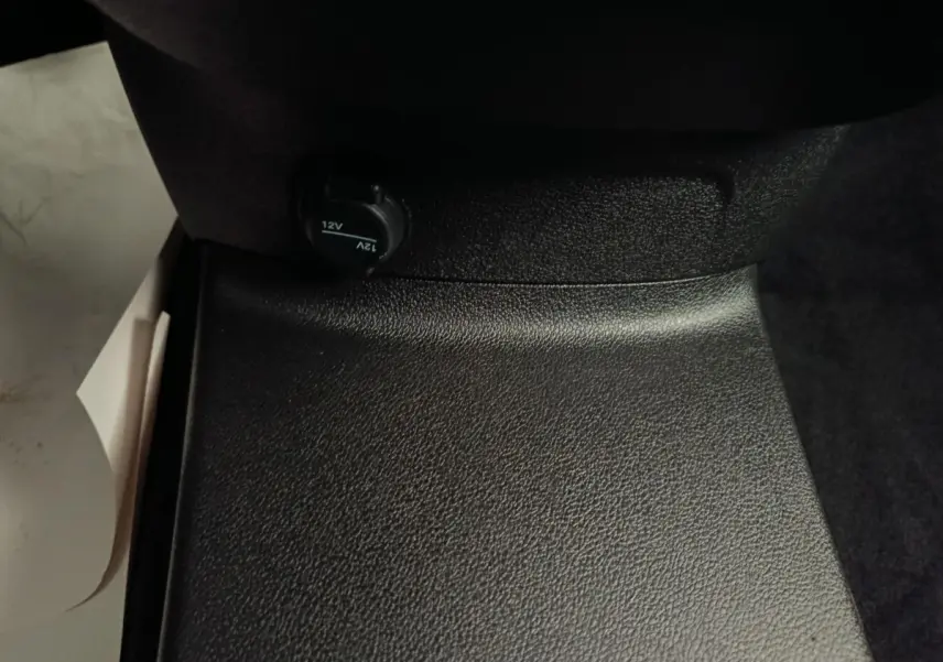 Prise 12V noire en gros plan sous le siège passager du Peugeot Partner blanc, vue intérieure rapprochée.